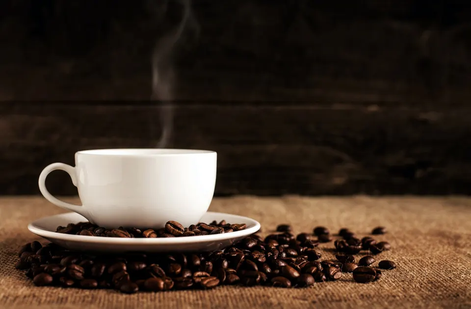 Image of a cup of coffee and coffee grains over a table