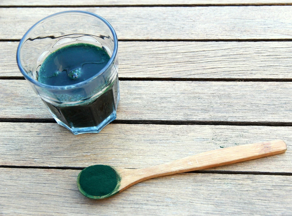 Image of spirulina on a table spoon and spirulina juice in a glass